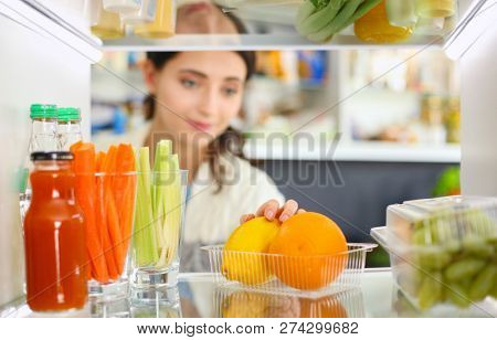 Portrait of female standing near open fridge full of healthy food, vegetables and fruits. Portrait of female