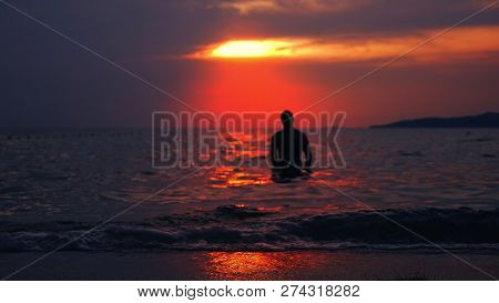 Silhouette Of A Fit Man Emerging From The Sea Against The Backdrop Of The Sea Landscape, A Red Drama