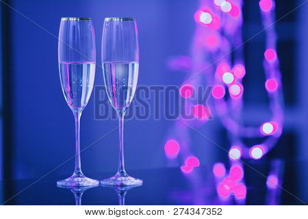 Holiday Pair Of Glasses Of Champagne In The Interior. Blurred Luminocity Neon Color Backdround. Chri