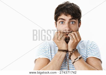 Young Worried Attractive Man With Wavy Hair Biting Fingernails Nervously, Widen Blue Eyes As Feeling