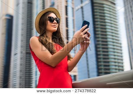 Portrait Of Young Smile Woman In Red Dress, Sunglasses And Summer Hat Typing Message Or Scroll Scree