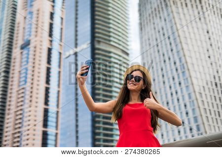 Portrait Of Young Smile Woman In Red Dress, Sunglasses And Summer Hat Make Video Call With Thumbs Up