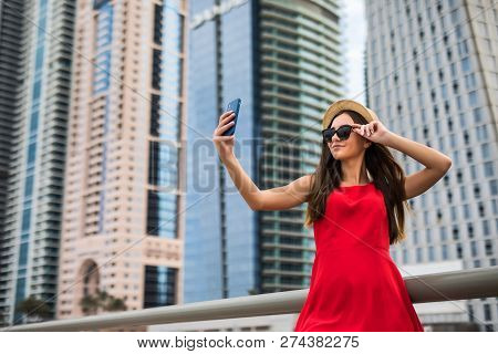 Portrait Of Young Smile Woman In Red Dress, Sunglasses And Summer Hat Make Selfie Or Video Call On T