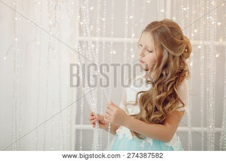 Little Princess Girl In Dress With Lush Light Blue Skirt, Beautiful Hair Curls, Stands On Background