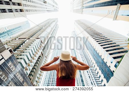 Rear View Of Young Woman In Red Dress Holding With Both Hands Straw Hat Amazed Looking Up On Skycrap