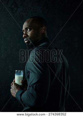 Healthy Young African Man Holging Cup Of Milk On A Bllack Studio Background.
