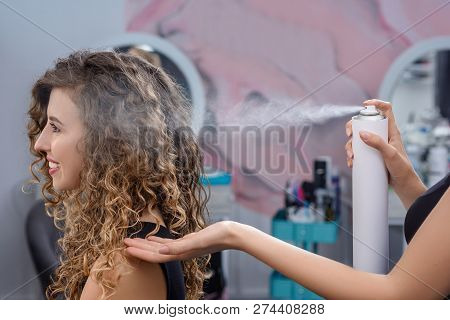 Side View Of Young Female Client Sitting In Chair In Beauty Salon While Stylist Fixing Hairstyle Wit