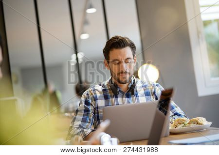 Attractive man eating sandwich whilst working in co working space