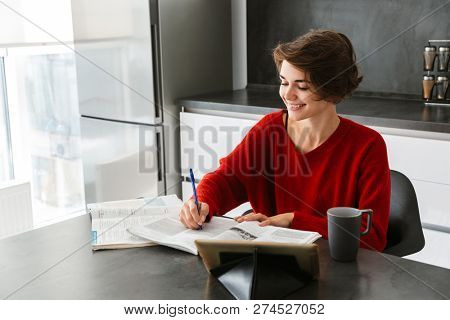 Smiling pretty young woman studying with a tablet computer at the table on a kitchen at home