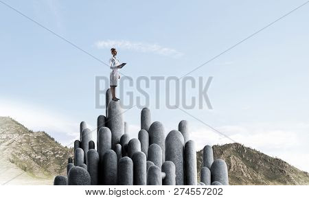 Young Female Doctor With Folder In Hands Satnding On Stone Column