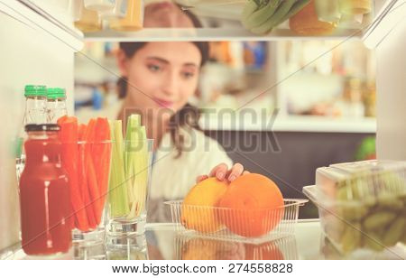 Portrait of female standing near open fridge full of healthy food, vegetables and fruits. Portrait of female