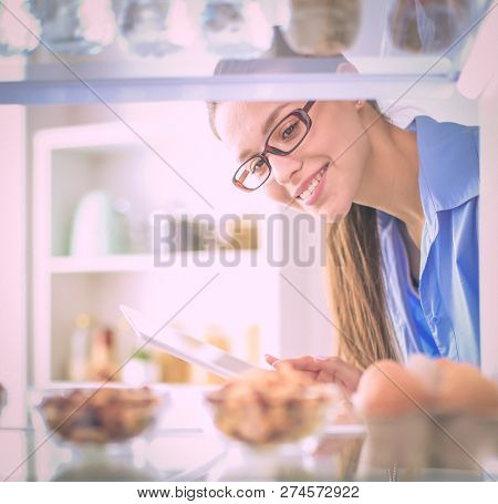 Portrait of female standing near open fridge full of healthy food, vegetables and fruits. Portrait of female