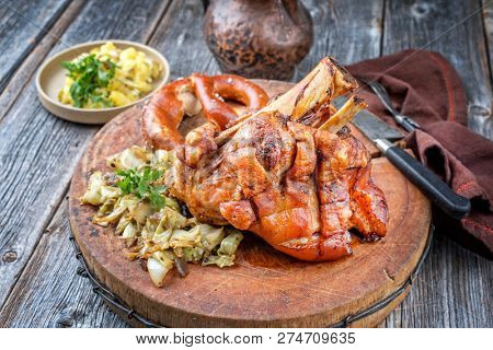 Traditional Bavarian schweinshaxe with coleslaw, potato salad and preztel as closeup on a wooden cutting board 