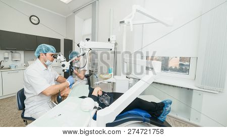 Doctor Used Microscope. Dentist Is Treating Patient In Modern Dental Office. Operation Is Carried Ou