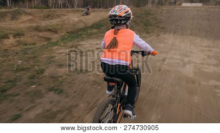 One Caucasian Children Rides Bike Road Track In Dirt Park. Girl Riding Black Orange Cycle In Racetra
