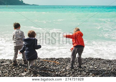 Three Children Pulling Pebbles In The Sea From The Beach During A Winter Day