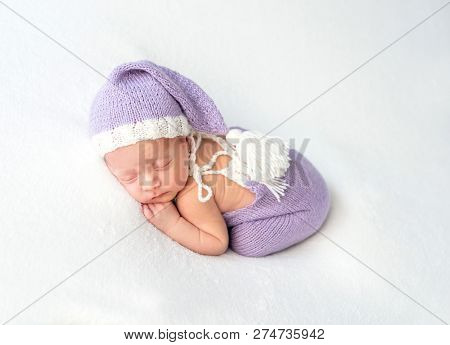 Cute little baby in white and purple knitted suit sweetly sleeping on white blanket
