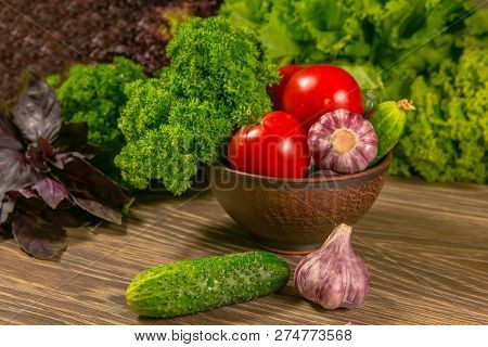 Tomatoes, Garlic Bulb And Cucumbers On A Wooden Table. Green Salad In The Background. The Concept Of