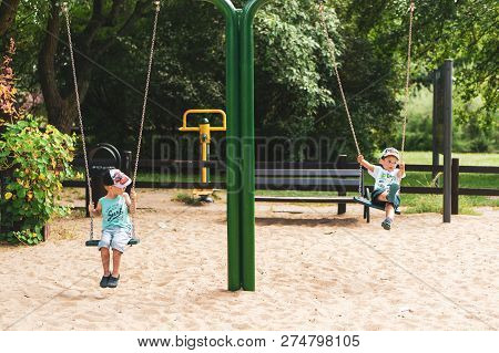 Poznan, Poland - July 29, 2018: Two Boy Sitting On A Swing At A Playground In The Cytadela Park. It 