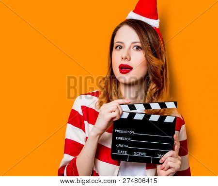 Portrait Of Young Redhead Woman In Santa Claus Hat And Striped Shirt With Filmmaking Clapperboard On