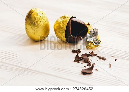 Happy Easter. Stylish Easter Chocolate Egg In Golden Foil And Broken Chocolate Egg On White Wooden B