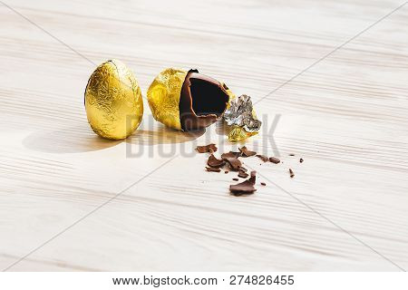 Stylish Easter Chocolate Egg In Golden Foil And Broken Chocolate Egg On White Wooden Background . Mo