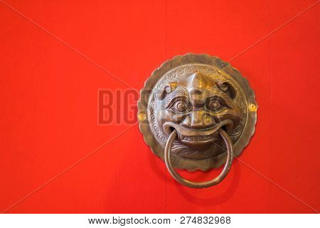 Red Wooden Door Of The Temple With The Brass Door Knocker.