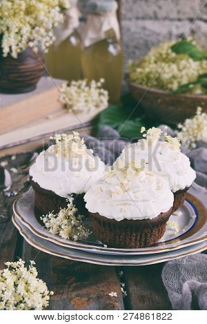 Chocolate Capcakes With Vanilla Cream Sprinkled With White Chocolate And Elderberry Flowers. Vintage