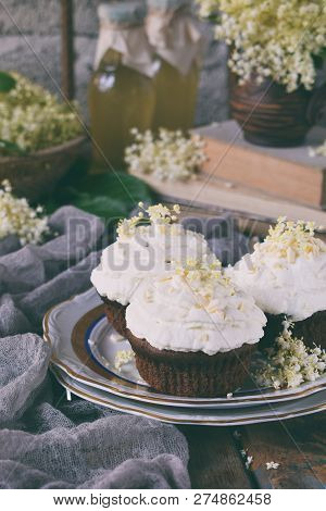 Chocolate Capcakes With Vanilla Cream Sprinkled With White Chocolate And Elderberry Flowers. Vintage