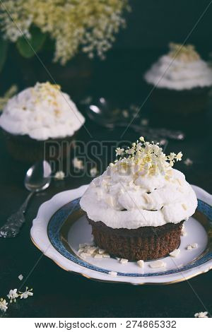 Chocolate Capcakes With Vanilla Cream Sprinkled With White Chocolate And Elderberry Flowers. Vintage