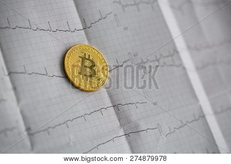 Bitcoin Is Alive. The Gold Coin Lies On A Paper Cardiogram Sheet Of People Heartbeat