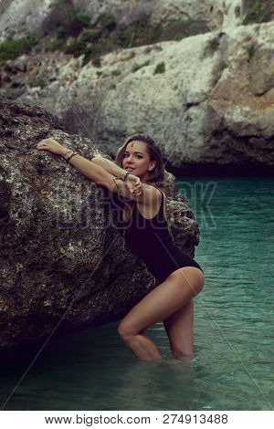 Young Beautiful Slylish Woman In Jewelry Posing In The Water Near The Rock. - Image