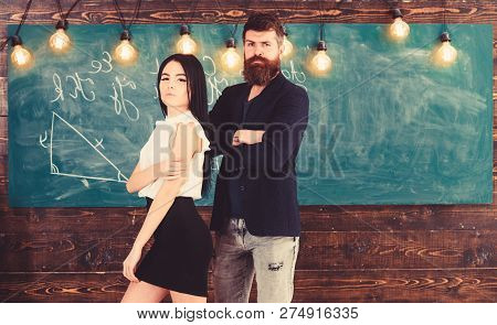 Partners Concept. Man With Beard And Sexy Girl Teacher Stand In Classroom, Chalkboard On Background.
