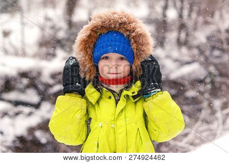 Cute Little Boy Walking Under The Snow. Happy Smiling Boy In Winter Clothes. Snowy Winter Weather. B
