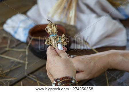 Hands Of An Elderly Woman Holding A Figure Of A Straw Man. Traditional Russian Folk Art