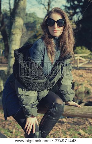 Attractive young woman wearing gray dress and hakki jacket with long fair hair posing outdoor in autunm or spring park over nature outdoor. Beautiful caucasian model portrait.