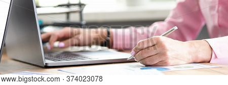 Hands Of An Office Employee Click On A Laptop Keyboard. Girl Sitting In The Office Makes Notes In A 