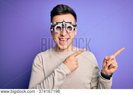 Young handsome caucasian man wearing optometrical glasses over purple background smiling and looking at the camera pointing with two hands and fingers to the side.