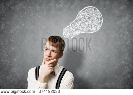 Redhead Student Thinking About Some Problem. Clever Boy On Background Of Grey Wall With Idea Lightbu