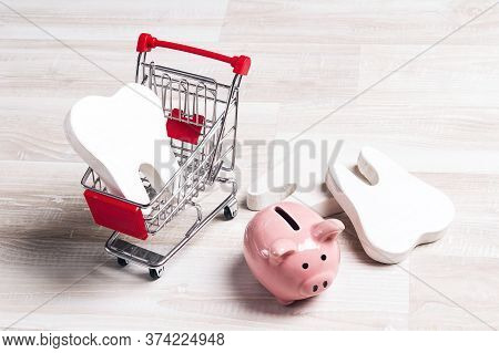 Pink Piggy Bank With Teeth In Shopping Trolley On A Light Wooden Background. Investing In Dental Hea