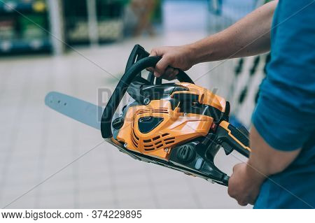 A Man Holds A Chain Saw In His Hand. A Buyer In A Hardware Store Selects A Product.