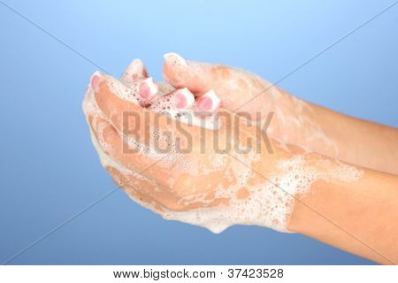ผู้หญิงมือใน soapsuds บนพื้นหลังสีฟ้าอย่างใกล้ชิด