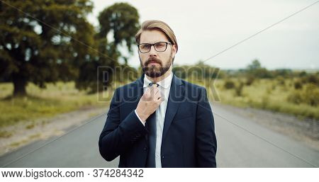 Half-body Portrait Of Businessman In Formal Attire Touching Tie Standing In Middle Of Country Road
