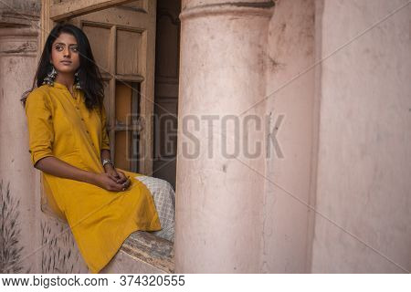 A Beautiful Asian Girl Sitting On The Window Wearing Indian Traditional Yellow Kurti With Beautiful