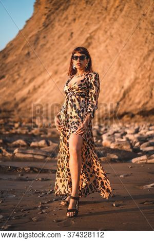 Summer Lifestyle On A Beach Next To Rocks Of A Young Brunette Caucasian Woman In A Leopard Dress By 