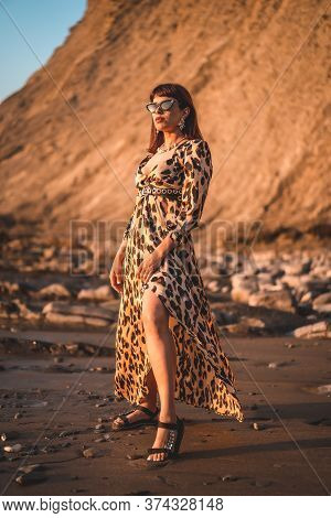 Summer Lifestyle On A Beach Next To Rocks Of A Young Brunette Caucasian Woman In A Leopard Dress By 