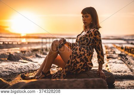 Summer Lifestyle On A Beach Next To Rocks Of A Young Brunette Caucasian Woman In A Leopard Dress By 