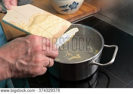 Cooking Spaetzle, Hands Of A Man Are Scraping  Homemade Egg Pasta Dough From A Wooden Board Into Boi