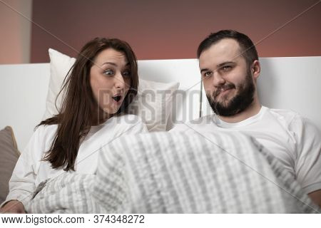 Beautiful Loving Married Couple Sitting In Bed. Boyfriend Raised Blanket Showing What Under It For E