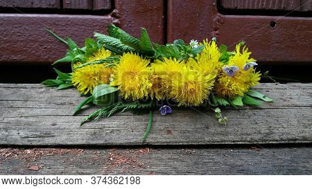A Wreath On The Head For A Girl From Wild Flowers. Dandelion Crown On The Background Of A Wooden Bui